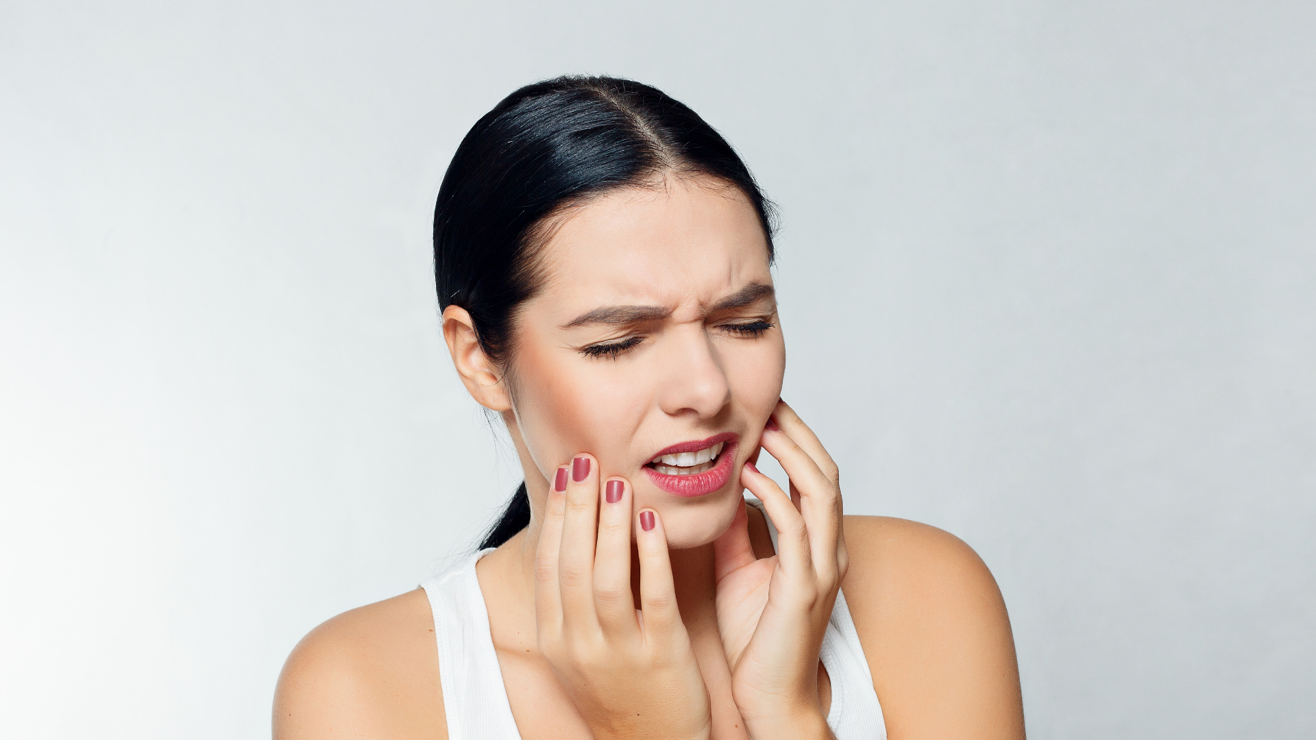 A woman with teeth pain holding her cheeks. Showing what happens when people don't wear their clear aligners as directed by professionals.